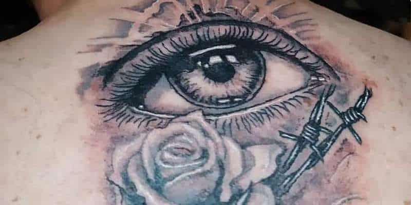 Photographie d'un tatouage, dans le haut du dos, motif un oeil, rune rose, des barbelés, une bougie